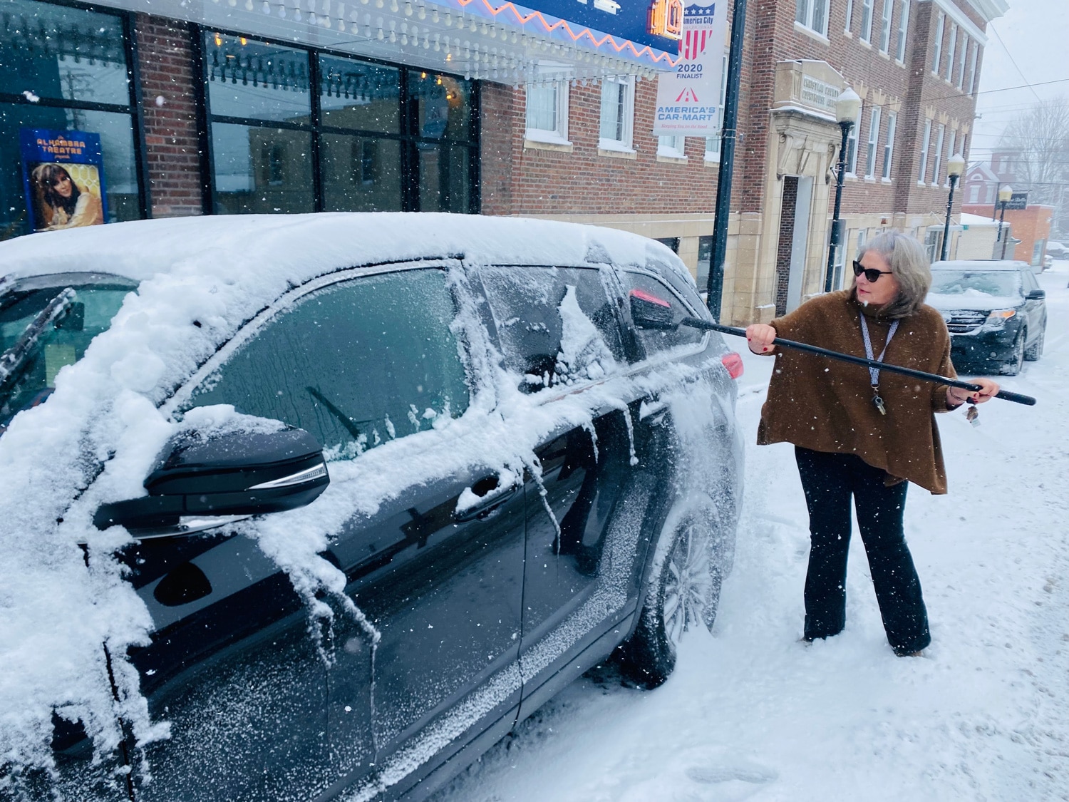 Margaret Prim, executive director of the Pennyroyal Arts Council, brushes snow off her car on Thursday, Jan. 6, 2022, in front of the Alhambra Theatre in Hopkinsville. (Photo by Jennifer P. Brown)