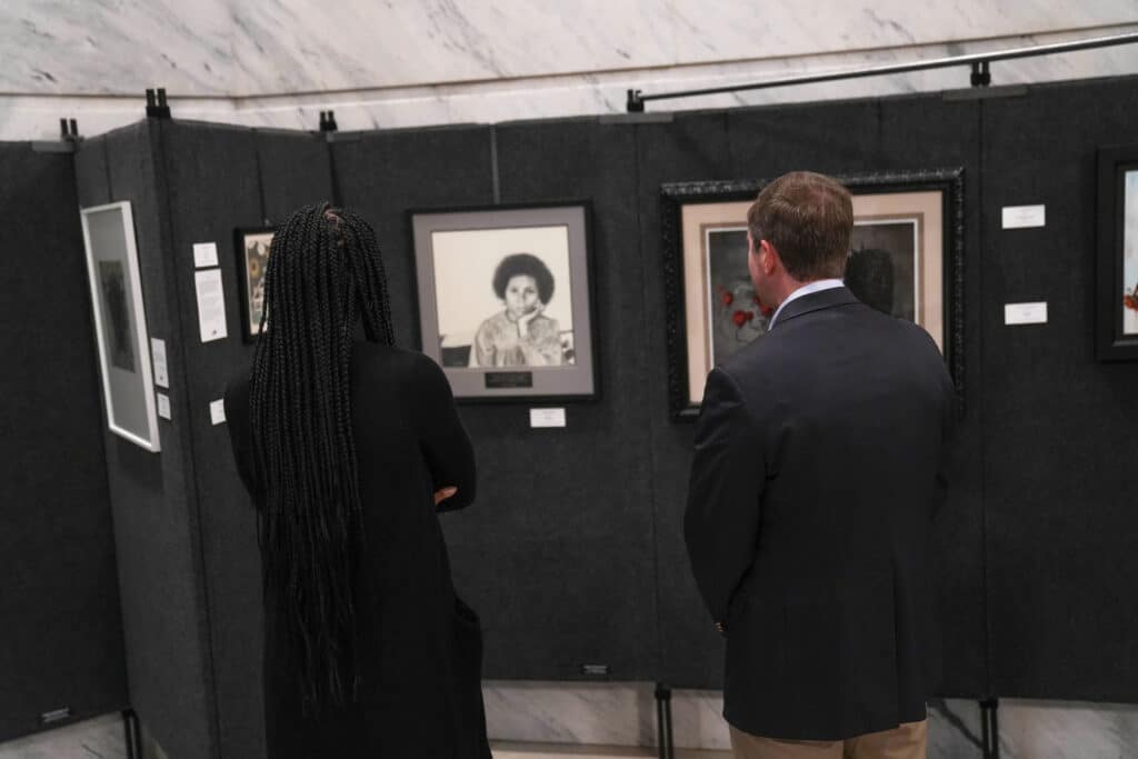 backs of Laurissa Kabithe and Andy Beshear looking at bell hooks portrait