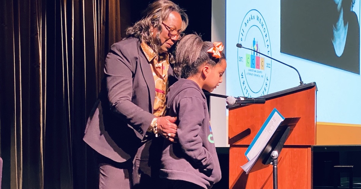 Christian County Literacy Council executive director Francene Gilmer helps Mariah Grace Gbemudu find her poem in a booklet so she can read it to an audience attending the bell hooks Writing Contest celebration of winners. (Hoptown Chronicle photo by Jennifer P. Brown)