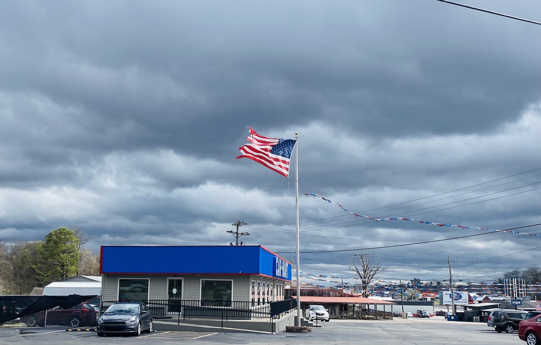 The March 3, 2023, storm whips an American flag on a car lot pole on Fort Campbell Boulevard near Walnut Street. (Hoptown Chronicle photo by Jennifer P. Brown)
