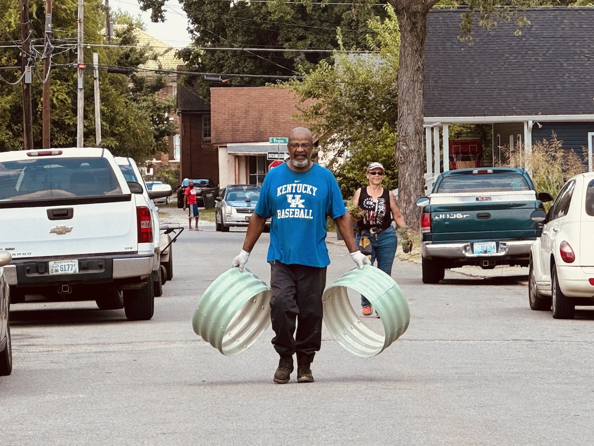 Durrett Avenue Neighborhood Association president Ardell Owens carries frames for small plant beds on Saturday, June 22, 2024, as he walks up Bryan Street. City Councilwoman Jamie Lienberger follows Owens with plants. (Hoptown Chronicle photo by Jennifer P. Brown)