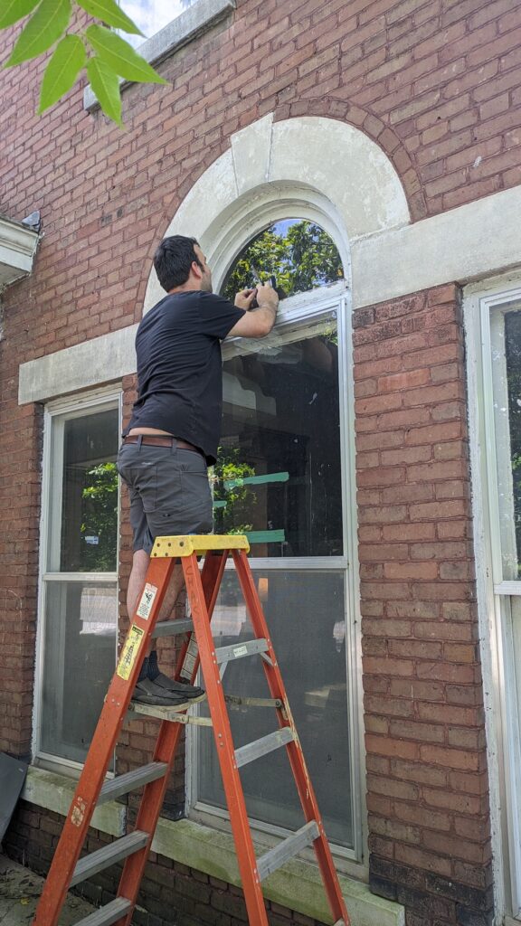 man on ladder repairing historic window