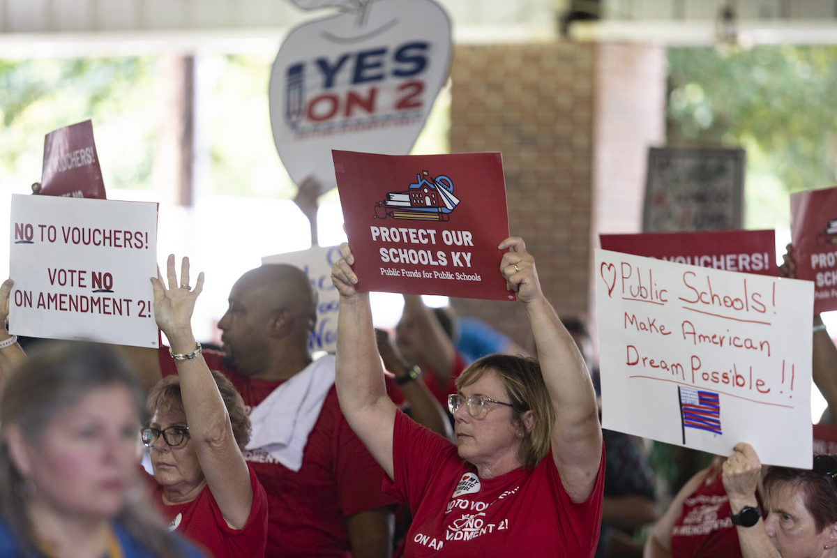 Signs hoisted Aug. 3, 2024, by members of the Fancy Farm audience express conflicting views on the school funding amendment that Kentucky voters will decide in November. (Kentucky Lantern photo by Austin Anthony)