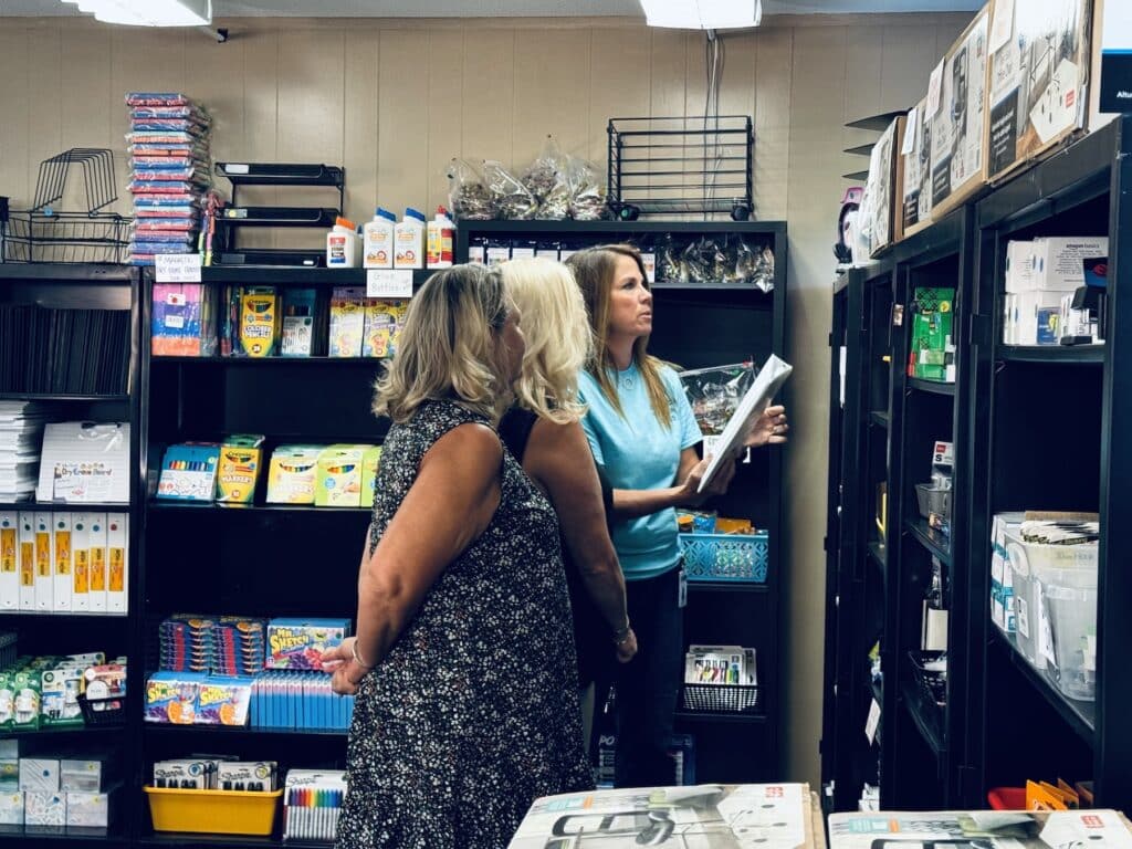 three women standing among teacher corner shelves