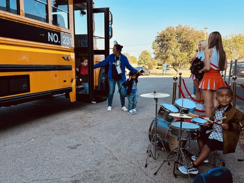 preschoolers stepping off bus to cheerleaders and young drummer