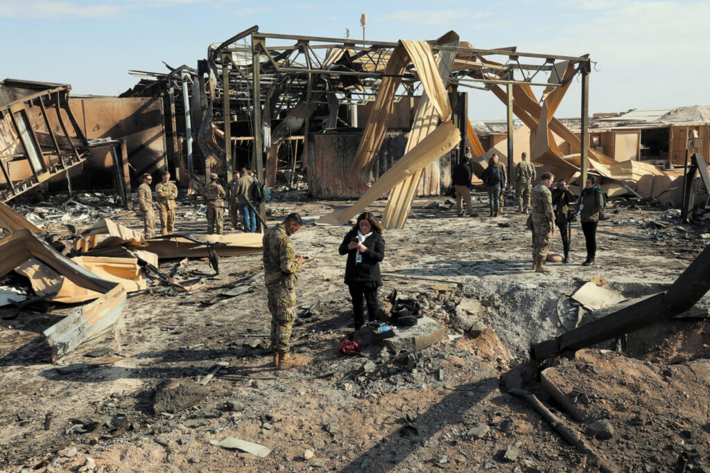 members of military and media in front of debris