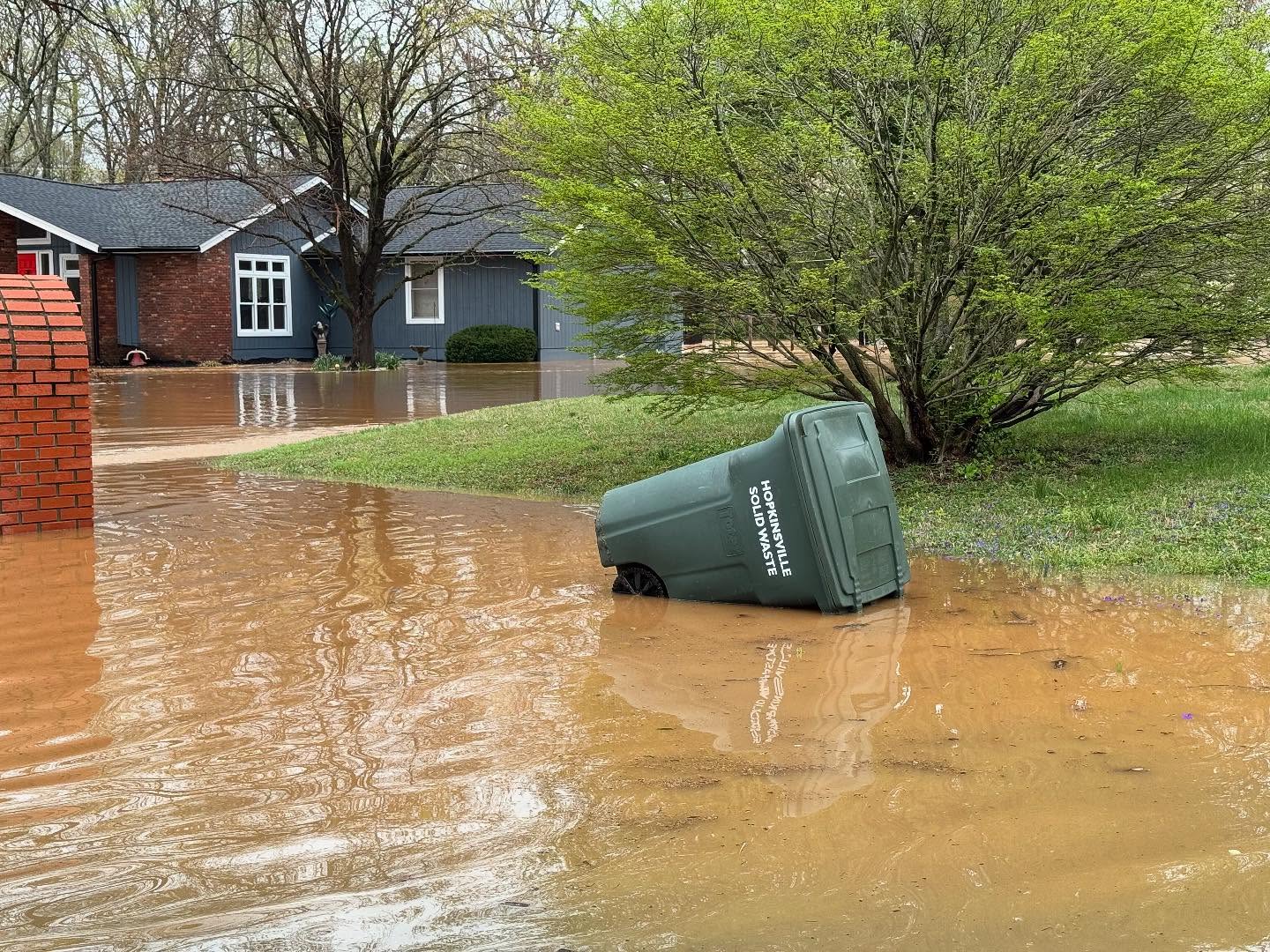 Herbie Curbie trash container floats in floodwater at the end of West Riverwood Drive on Friday, April 4, 2025. (Hoptown Chronicle photo by Jennifer P. Brown)