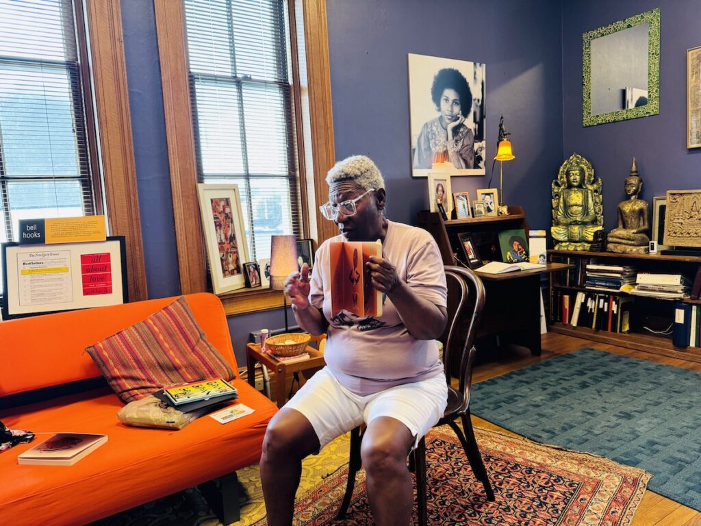 woman sitting in chair and holding book in room with bell hooks photos and mementos