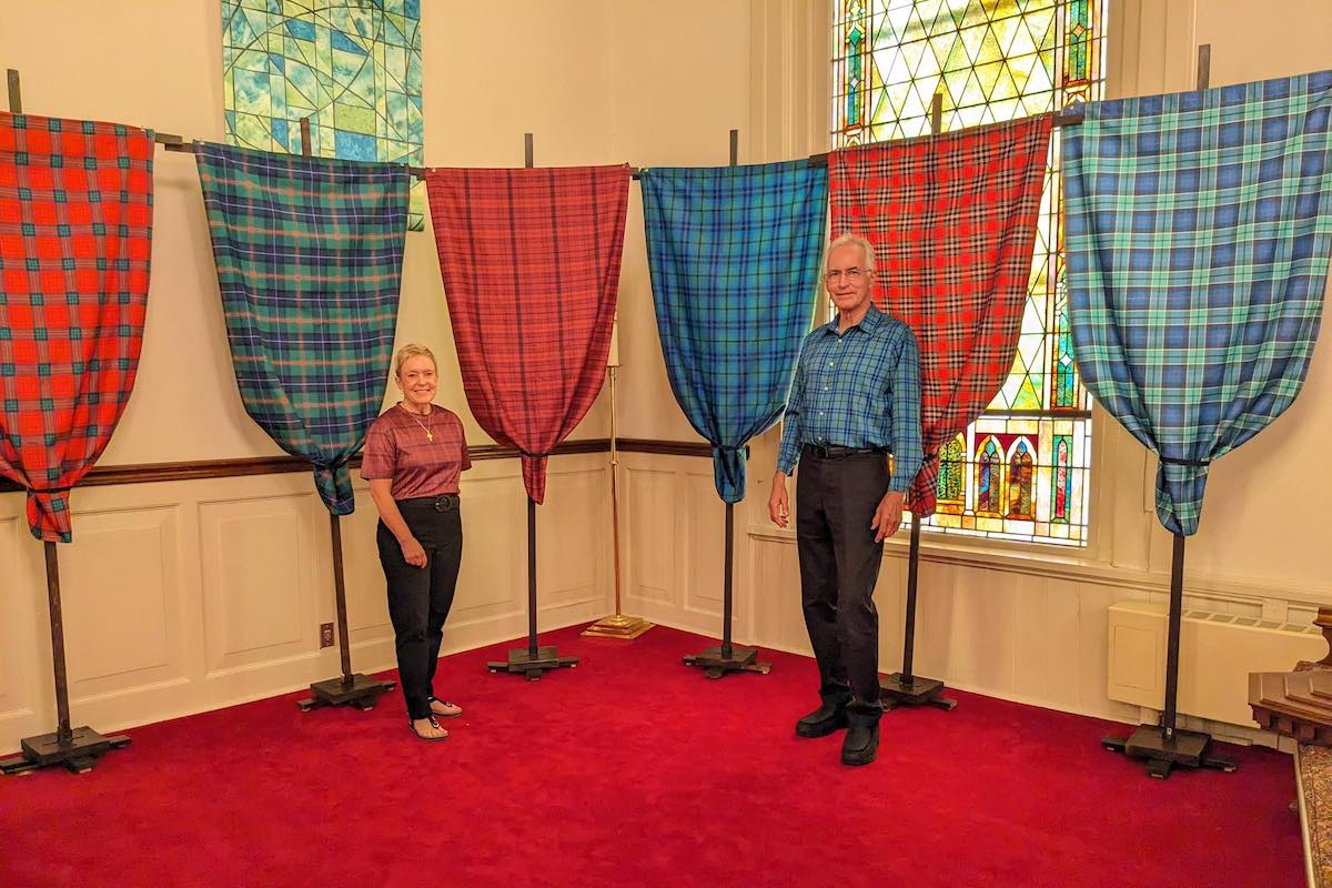 Kat and Bob Sholly stand in front of some of the tartans prepared for a procession on Sunday, Oct. 26, at First Presbyterian Church. (Church photo by Janet Bravard)