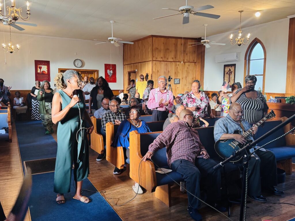 woman singing with people sitting and standing in church pews