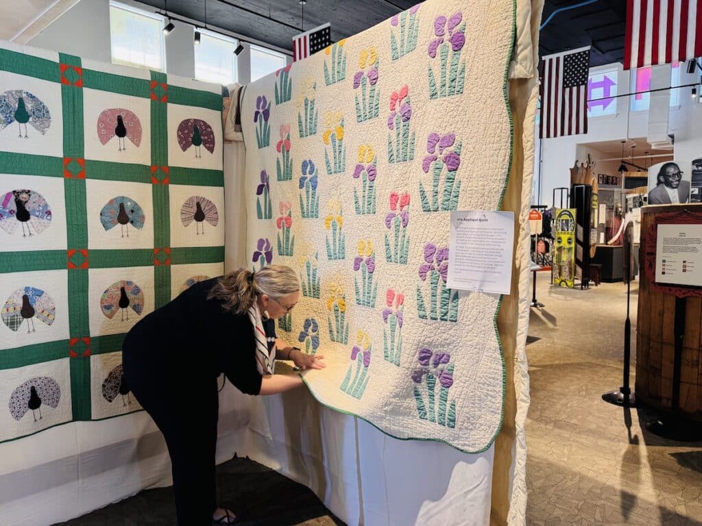 woman adjusting quilt on display at museum