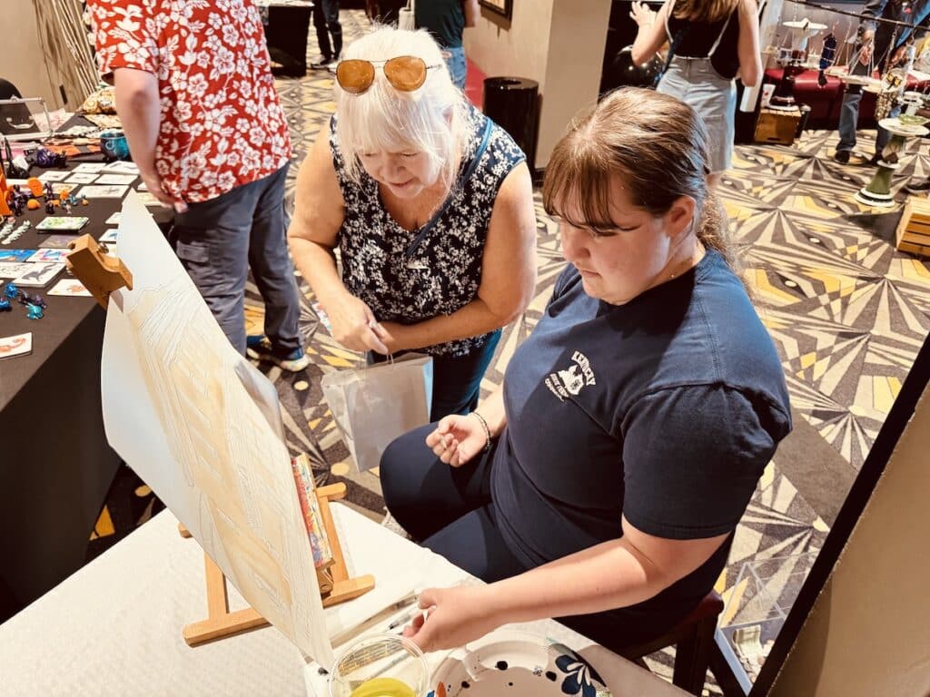 two women looking at painting on easel