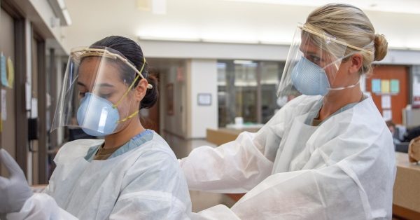 SAN DIEGO (Aug. 4, 2020) Ensign Kaitlyn Leibing, right, a staff nurse assigned to one of Naval Medical Center San Diego’s (NMCSD) internal medicine wards, helps Hospitalman Angela Mello, a general duty corpsman assigned to  NMCSD, don personal protective equipment (PPE), including a 3D-printed face shield donated to the hospital by Naval Information Warfare Systems Command, before entering a COVID-19-positive, non-critical patient’s room, Aug. 4, 2020. Face shields, N95 respirator masks, gloves and gowns are some of the PPE required to enter COVID-19-patient spaces. NMCSD’s mission is to prepare service members to deploy in support of operational forces, deliver high quality healthcare services and shape the future of military medicine through education, training and research. NMCSD employs more than 6,000 active duty military personnel, civilians, and contractors in Southern California to provide patients with world-class care anytime, anywhere. (U.S. Navy photo by Mass Communication Specialist 3rd Class Jake Greenberg) 200804-N-DA693-1016