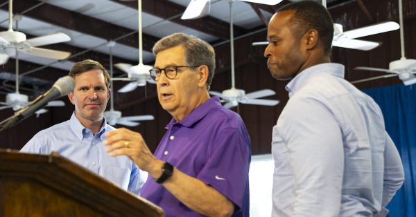 Gov. Andy Beshear and candidate Daniel Cameron with emcee David Beck on Saturday, Aug. 5, at the Fancy Farm Picnic. (Kentucky Lantern photo by Austin Anthony)