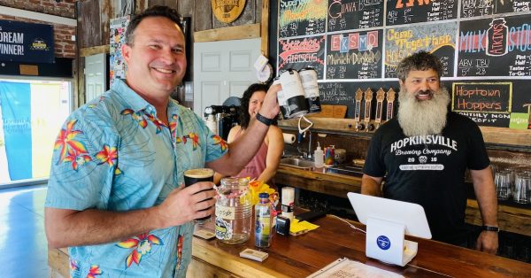 Daniel Brechwald lifts a four-pack and a pint of stout after purchasing the first Sunday alcohol sold at Hopkinsville Brewing Co. on May 29, 2022. Brewery owners Kate Russell and Joey Medeiros celebrated the moment with Brechwald. (Photo by Jennifer P. Brown)