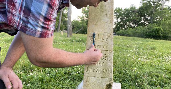 Brendan Abernethy uses a toothbrush to scrub in the inscribed name of Belle Watts during a tombstone cleaning activity Tuesday, May 30, 2023, at Union Benevolent Society Cemetery. (Hoptown Chronicle photo by Jennifer P. Brown)