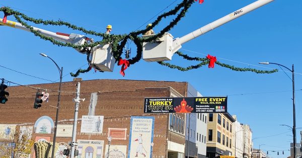 Two workers in utility truck buckets hang Christmas garland on Nov. 15, 2023, above the intersection of Ninth and Main streets. (Hoptown Chronicle photo by Jennifer P. Brown)