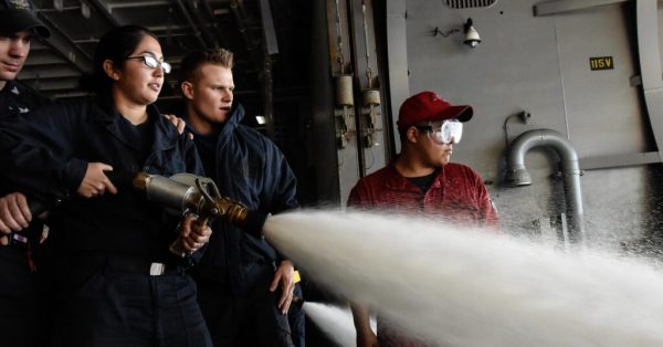 Sailors operate a fire hose while spraying Aqueous Film Forming Foam during a test of firefighting equipment aboard the aircraft carrier USS Theodore Roosevelt on Dec. 19, 2016. (Photo U.S. Navy photo by Petty Officer 3rd Class Jimmi Lee Bruner | CC BY-NC 2.0 DEED)