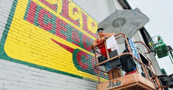 Paula Gieseke worked from a lift to recreate the old Ellis Ice and Coal Co. sign and also to paint a new mural of the American flag in July 2024 on another section of the HWEA building on 11th and Clay streets. (Hoptown Chronicle photos by Jennifer P. Brown)