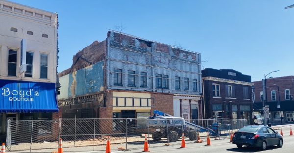 South Main Street traffic on Tuesday, Feb. 28, 2023, passes fencing and a boom lift in front of the Holland Opera House. The second-story windows on the opera house were revealed for the first time in decades following removal of a metal facade on the building that is being demolished. (Hoptown Chronicle photo by Jennifer P. Brown)