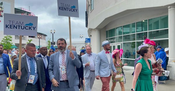 A train of people following Team Kentucky signs walk pass the paddock area of Churchill Downs. Team Kentucky is a Beshear administration slogan. (Kentucky Lantern photo by McKenna Horsley)